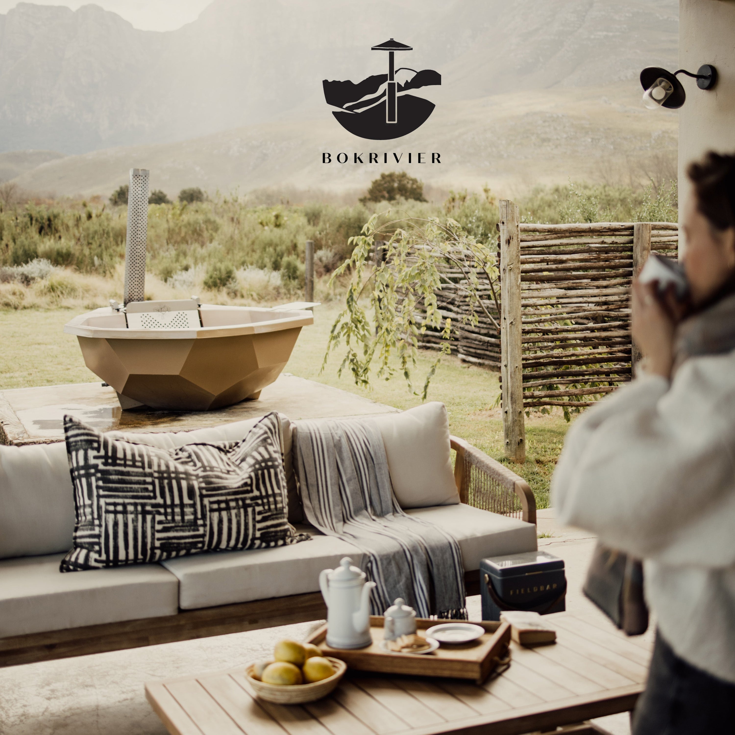 Outdoor living space with a hot tub, couch, and coffee table in a scenic setting.